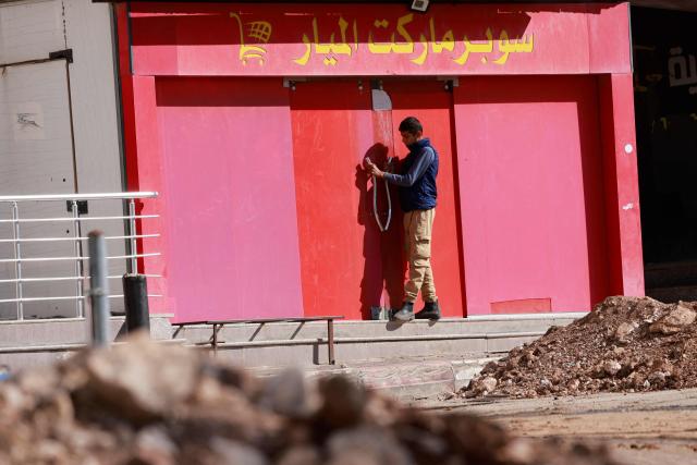 A Palestinian man stands next to a closed shop due to a curfew imposed during an Israeli military operation in the city of Tubas, north of the occupied West Bank, on December 1, 2025. Israel's military launched a new operation against Palestinian armed groups in the occupied West Bank, where a local governor told AFP that Israeli forces had raided several towns. (Photo by Jaafar ASHTIYEH / AFP)