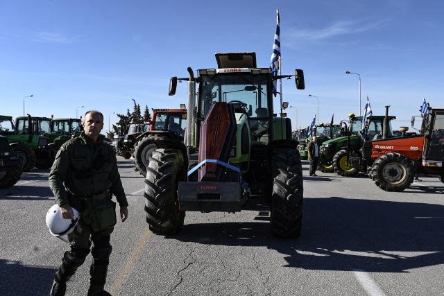 A policeman in riot gear walks pasr tractors blocking a national highway during a farmers' protest over the reduced and delayed payment of European Union subsidies, at the Malgara tolls near Thessaloniki on December 1, 2025. (Photo by Sakis Mitrolidis / AFP)