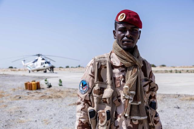 A Chadian soldier from the anti-terrorist unit poses in front of a Multinational Joint Task Force (MNJTF) helicopter at the Baga Sola military base, Lake Chad Province, Chad, on 26 November, 2025. The new commander-in-chief of the Multinational Joint Task Force (MNJTF) for counter-jihadist efforts in the Lake Chad Basin assured on Wednesday to AFP that securing waterways is a priority mission in this border region of Central Africa. Establishing secure navigation corridors is "one of the main priorities," according to General Saidou Tanko Audu, who has been leading the regional counter-jihadist force since mid-November. (Photo by Joris Bolomey / AFP)