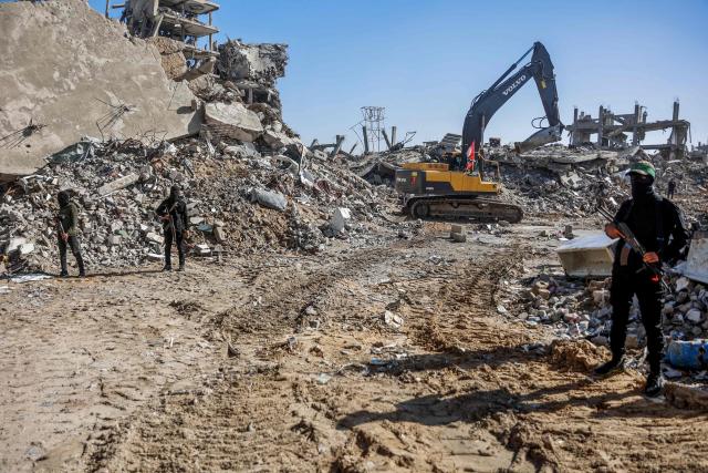 Palestinian Hamas militants stand guard as Egyptian workers accompanied by members of the International Committee of the Red Cross (ICRC), unseen, use a digger as they search for the last two remaining bodies of hostages in Jabalia refugee camp, in the northern of Gaza Strip on December 1, 2025. The Gaza war was sparked by Hamas's October 7, 2023 attack on Israel, resulting in the deaths of 1,221 people and the taking 251 hostage. Israel's retaliatory assault on Gaza has killed over 70,000 people, according to figures from the health ministry that the UN considers reliable. (Photo by Omar AL-QATTAA / AFP)