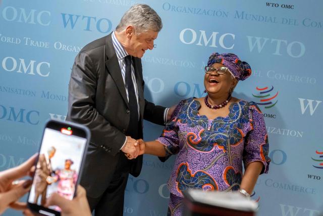 France's junior Minister in charge of external trade Nicolas Forissier (L) and World Trade Organization (WTO) Director-General Ngozi Okonjo-Iweala react as they shake hands after a meeting at the WTO's headquarters in Geneva on December 1, 2025. (Photo by Fabrice COFFRINI / AFP)