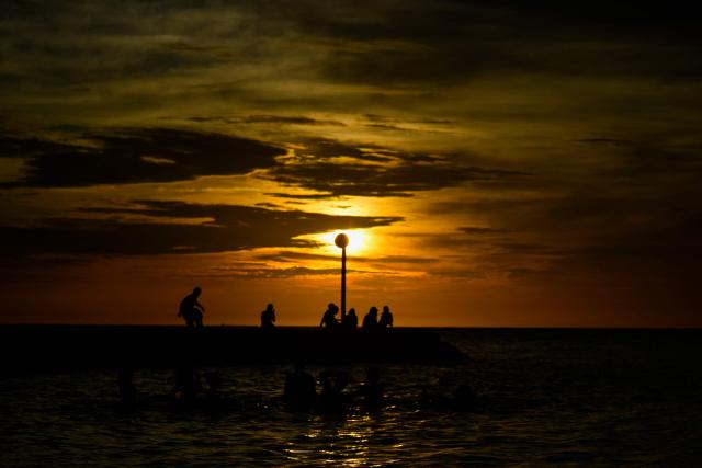 View or people's silhouettes during sunset at Rodadero Beach in Santa Marta, Colombia, on November 30, 2025. (Photo by Diana SANCHEZ / AFP)