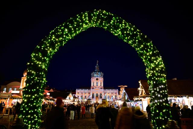 Visitors walk between stalls at the Christmas market in front of the illuminated Charlottenburg Palace in Berlin on December 1, 2025. (Photo by Tobias SCHWARZ / AFP)