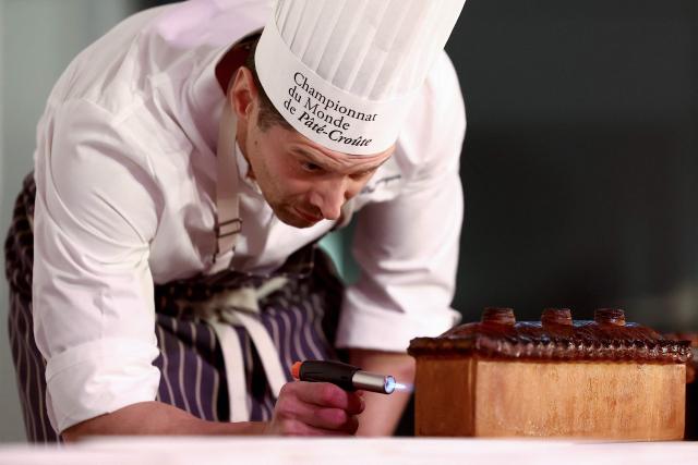 French chef Nicolas Delaroque representing Canada and the US, uses a cooking torch for the last finishing touches on his pate-croute creation during the 16th Edition of the 2025 Pate-Croute World Championship, in Lyon, central-eastern France, on December 1, 2025. (Photo by Alex MARTIN / AFP)