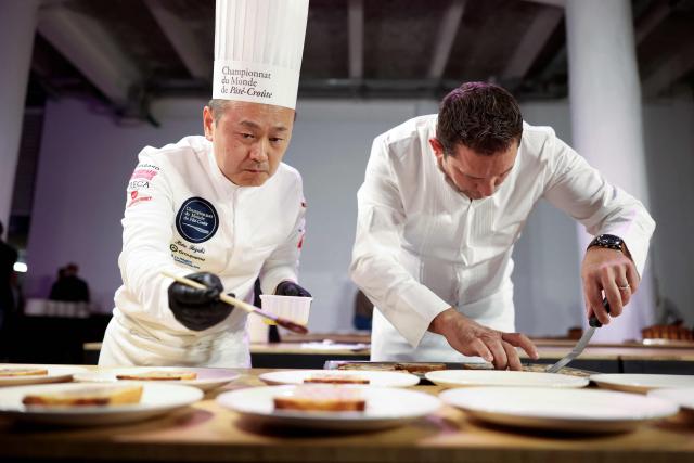 Japanese chef Kota Suzuki (L) representing Monaco, prepares the dishes with his pate-croute creation during the 16th Edition of the 2025 Pate-Croute World Championship, in Lyon, central-eastern France, on December 1, 2025. (Photo by Alex MARTIN / AFP)