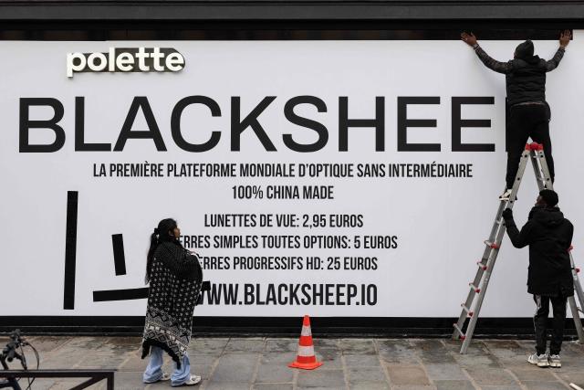 Workmen adjust signage on the facade of a future discount eyeglasses Blacksheep retail shop, on Paris' shopping high street Rue de Rivoli, on December 1, 2025. (Photo by Ian LANGSDON / AFP)