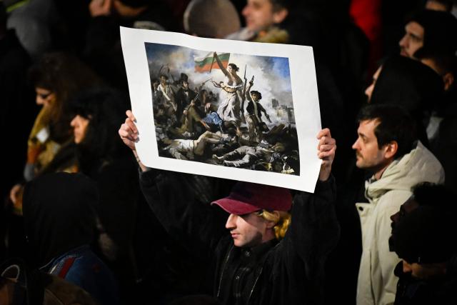 A protester holds a placard with the painting of Eugene Delacroix 'Liberty Leading the People', with the Bulgarian flag instead of the French one, during an anti-government protest in Sofia on December 1, 2025. Tens of thousands of people held anti-government protests in Bulgaria on Monday, widening an anti-corruption movement sweeping the European Union's poorest country as it prepares to adopt the euro. (Photo by Nikolay DOYCHINOV / AFP)