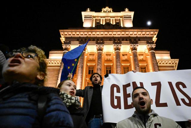 A protester holds the EU flag and a banner about the 'Gen Z' during an anti-government protest at teh Independence Square in Sofia on December 1, 2025. Tens of thousands of people held anti-government protests in Bulgaria on Monday, widening an anti-corruption movement sweeping the European Union's poorest country as it prepares to adopt the euro. (Photo by Nikolay DOYCHINOV / AFP)