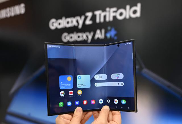 A visitor holds a Samsung Galaxy Z TriFold smartphone during a launch event at a Samsung store in Seoul on December 2, 2025. Samsung Electronics unveiled its first tri-fold phone on December 2, as the conglomerate rushes to show it can keep pace with rivals in generative AI. (Photo by Jung Yeon-je / AFP)