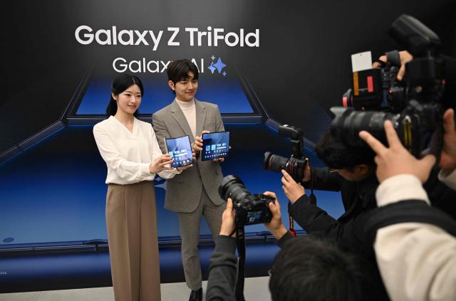 Promoters show Samsung Galaxy Z TriFold smartphones to photographers during a launch event at a Samsung store in Seoul on December 2, 2025. Samsung Electronics unveiled its first tri-fold phone on December 2, as the conglomerate rushes to show it can keep pace with rivals in generative AI. (Photo by Jung Yeon-je / AFP)