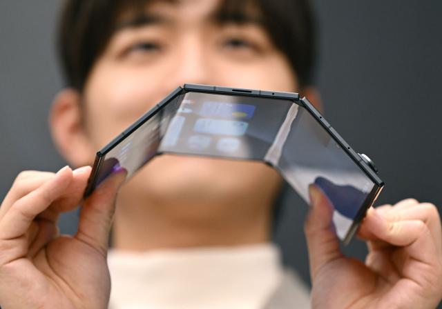 A promoter shows a Samsung Galaxy Z TriFold smartphone during a launch event at a Samsung store in Seoul on December 2, 2025. Samsung Electronics unveiled its first tri-fold phone on December 2, as the conglomerate rushes to show it can keep pace with rivals in generative AI. (Photo by Jung Yeon-je / AFP)