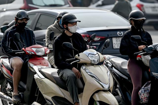 Motorists on scooters wear face masks on a street during heavy air pollution conditions in Hanoi on December 2, 2025. (Photo by Nhac NGUYEN / AFP)
