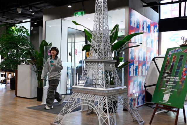 A woman walks past a model of Eiffel Tower at the Institut Francais in Beijing on December 2, 2025. (Photo by WANG Zhao / AFP)