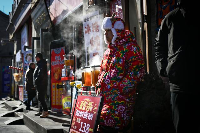 A sales guide waits for customers by the entrance of a restaurant in Beijing on December 2, 2025. (Photo by WANG Zhao / AFP)