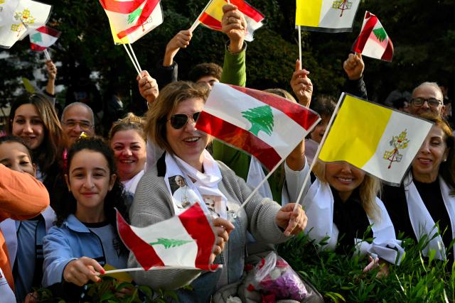 People waves flags on the side of the road before the visit of Pope Leo XIV to the Sisters of the Cross Hospital in Beirut's northern suburb of Jdeideh, on December 2, 2025.  (Photo by Andreas SOLARO / AFP)