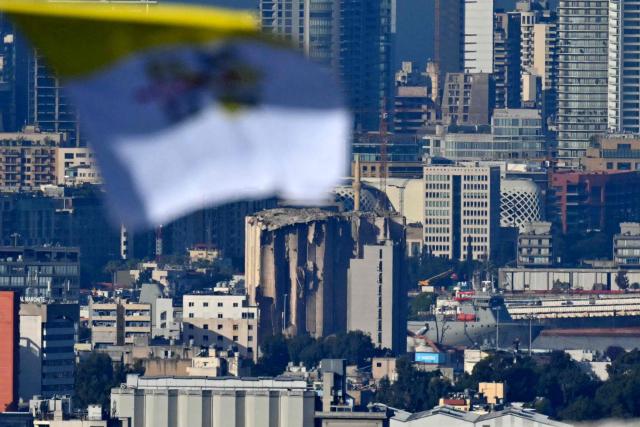 A Vatican's flag flies outside the Sisters of the Cross Hospital with dammaged building of the port in the background, in Beirut's northern suburb of Jdeideh before the visit of Pope Leo XIV on December 2, 2025.  (Photo by Andreas SOLARO / AFP)