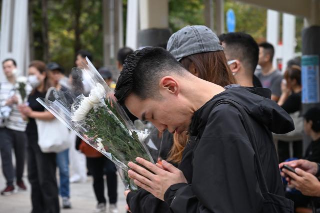 People pray and leave flowers for the victims outside the Wang Fuk Court apartment blocks in the aftermath of the deadly November 26 fire in Hong Kong's Tai Po district on December 2, 2025. Hong Kong's leader announced on December 2 the creation of a judge-led "independent committee" to investigate the devastating fire at an apartment complex that killed 151 people last week. Authorities have said the blaze, which was the city's worst fire in decades, spread quickly via netting used on exterior scaffolding that fell short of fire-resistance standards and failed to stop flames from spreading. (Photo by Peter PARKS / AFP)