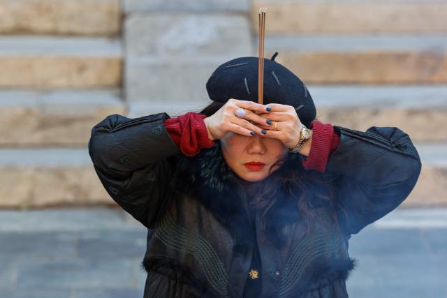 A woman burns incense and prays at the Lama Temple in Beijing on December 2, 2025. (Photo by Ludovic MARIN / AFP)