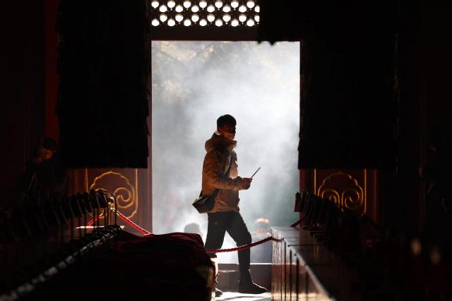 A man burns incense and prays at the Lama Temple in Beijing on December 2, 2025. (Photo by Ludovic MARIN / AFP)