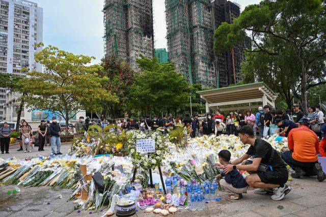 People leave flowers for the victims outside the Wang Fuk Court apartment blocks in the aftermath of the deadly November 26 fire in Hong Kong's Tai Po district on December 2, 2025. Hong Kong's leader announced on December 2 the creation of a judge-led "independent committee" to investigate the devastating fire at an apartment complex that killed 151 people last week. Authorities have said the blaze, which was the city's worst fire in decades, spread quickly via netting used on exterior scaffolding that fell short of fire-resistance standards and failed to stop flames from spreading. (Photo by Peter PARKS / AFP)