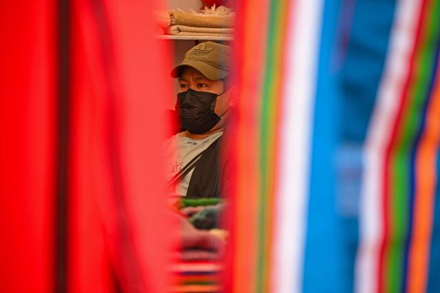 A shopkeeper wearing a face mask sits inside an apparel store in New Delhi on December 2, 2025. (Photo by Sajjad HUSSAIN / AFP)