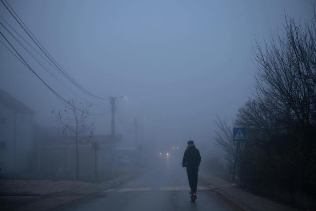 A resident rides an electric scooter through thick smog in Pristina on December 2, 2025. (Photo by Armend NIMANI / AFP)