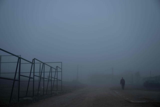A resident walks through thick smog in Pristina on December 2, 2025. (Photo by Armend NIMANI / AFP)