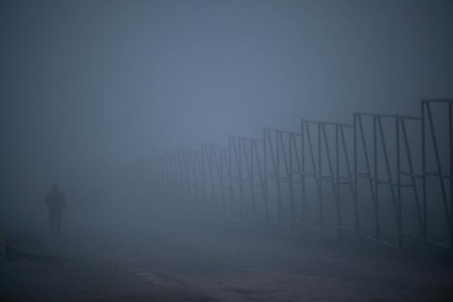 A resident walks through thick smog in Pristina on December 2, 2025. (Photo by Armend NIMANI / AFP)