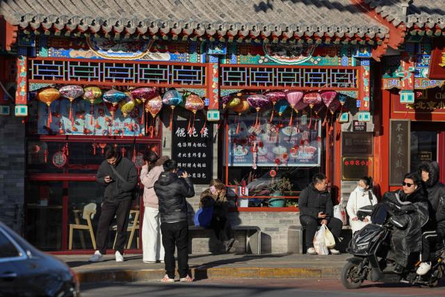 People are seen on a street in Beijing on December 2, 2025. (Photo by Ludovic MARIN / AFP)