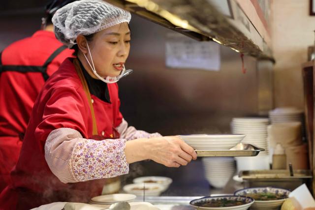 A woman serves food at a restaurant in Beijing on December 2, 2025. (Photo by Ludovic MARIN / AFP)