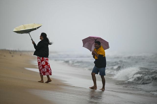 People clutch onto their umbrellas during rain and high tides induced by Cyclone Ditwah at the Marina beach in Chennai on December 2, 2025. (Photo by R. Satish BABU / AFP)