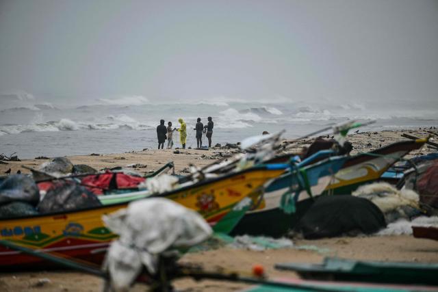Fishermen stand near boats docked at the Marina beach during high tides induced by Cyclone Ditwah in Chennai on December 2, 2025. (Photo by R. Satish BABU / AFP)