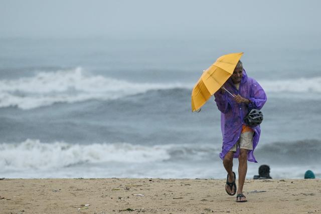 A man clutches onto his umbrella during rain and high tides induced by Cyclone Ditwah at the Marina beach in Chennai on December 2, 2025. (Photo by R. Satish BABU / AFP)