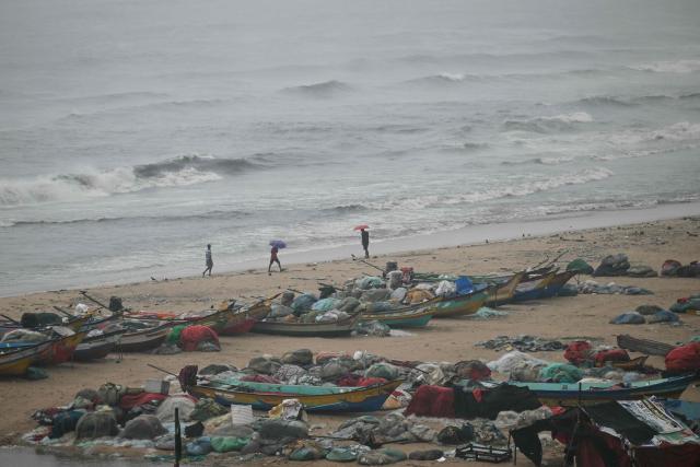 People stand near boats docked at the Marina beach during high tides induced by Cyclone Ditwah in Chennai on December 2, 2025. (Photo by R. Satish BABU / AFP)