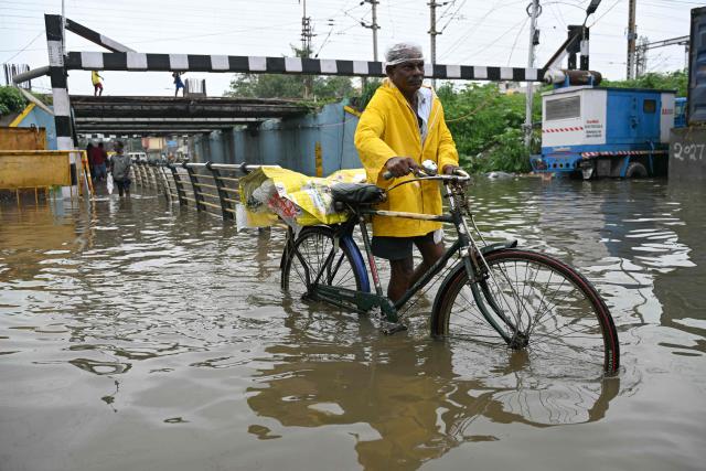 A man wades through floodwaters induced by Cyclone Ditwah, near a railway bridge in Chennai on December 2, 2025. (Photo by R. Satish BABU / AFP)