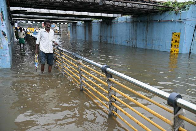 A man wades through floodwaters induced by Cyclone Ditwah, under a railway bridge in Chennai on December 2, 2025. (Photo by R. Satish BABU / AFP)