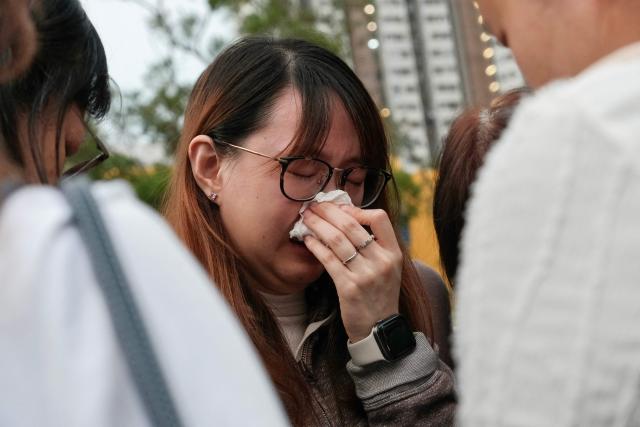 A mourner weeps outside the Wang Fuk Court apartment blocks in the aftermath of the deadly November 26 fire in Hong Kong's Tai Po district on December 2, 2025. Hong Kong's leader announced on December 2 the creation of a judge-led "independent committee" to investigate the devastating fire at an apartment complex that killed 151 people last week. Authorities have said the blaze, which was the city's worst fire in decades, spread quickly via netting used on exterior scaffolding that fell short of fire-resistance standards and failed to stop flames from spreading. (Photo by Tommy WANG / AFP)