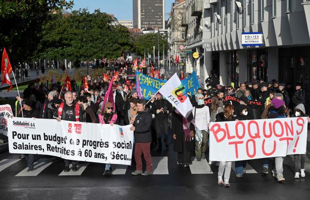 Protesters hold banners reading 'For a budget for social progress, wages, retirement at 60, social security' and 'let's block everything' during a demonstration as part of a call by trade unions for strikes and demonstrations for higher wages and against austerity, in Nantes, western France, on December 2, 2025. (Photo by Sebastien Salom-Gomis / AFP)