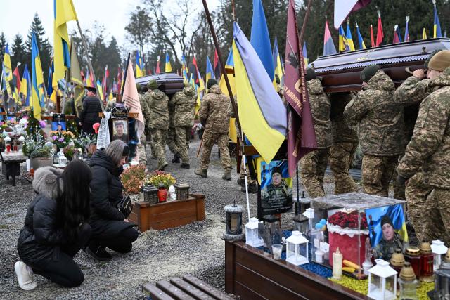 Mourners knee as Ukrainian soldiers carry the coffins of Ukrainian servicemen Marian Maksymiv and Andriy Dobryansky during a funeral ceremony at the Lychakiv military cemetery in Lviv on December 2, 2025, amid the Russian invasion of Ukraine. (Photo by Sergei GAPON / AFP)