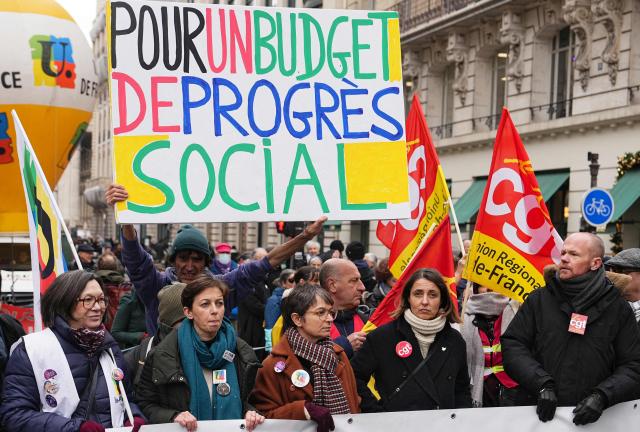 French trade union General Confederation of Labour (CGT) secretary general Sophie Binet (2nd R) looks on flanked by protesters as they stand before a placard reading "For a social progress budget" and take part in a demonstration as part of a call by trade unions for strikes and demonstrations for higher wages and against austerity, in Paris on December 2, 2025. (Photo by Dimitar DILKOFF / AFP)
