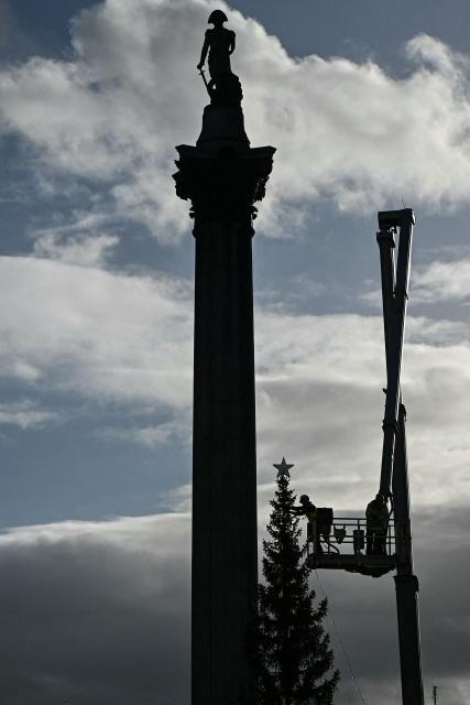 A worker (C) on an elevated work platform makes adjustments to a large Christmas tree erected in Trafalgar Square, next to Nelson's Column, in central London on December 2, 2025. (Photo by JUSTIN TALLIS / AFP)