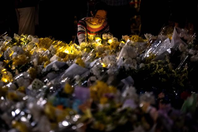 A woman offers flowers during a vigil held outside the Wang Fuk Court apartment blocks in the aftermath of the deadly November 26 fire in Hong Kong's Tai Po district on December 2, 2025. Hong Kong's leader said on December 2 that an independent committee will investigate the causes of the city's deadliest fire in decades, after authorities found substandard building materials had accelerated the blaze. The fire engulfed seven residential towers under renovation in the north of the city last week, killing at least 156 people, displacing thousands more and fuelling public demands for accountability. (Photo by Philip FONG / AFP)