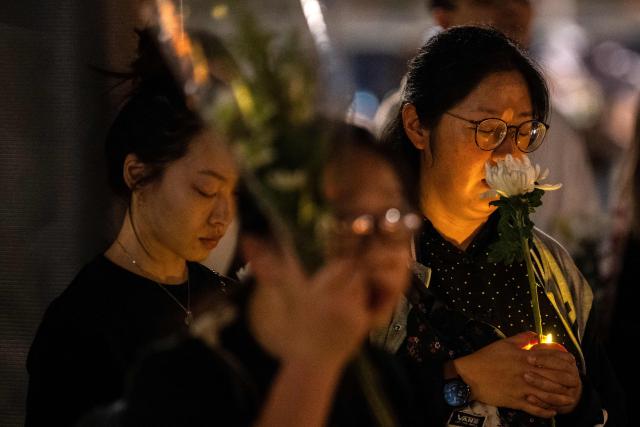People pray with flowers during a vigil held outside the Wang Fuk Court apartment blocks in the aftermath of the deadly November 26 fire in Hong Kong's Tai Po district on December 2, 2025. Hong Kong's leader said on December 2 that an independent committee will investigate the causes of the city's deadliest fire in decades, after authorities found substandard building materials had accelerated the blaze. The fire engulfed seven residential towers under renovation in the north of the city last week, killing at least 156 people, displacing thousands more and fuelling public demands for accountability. (Photo by Philip FONG / AFP)