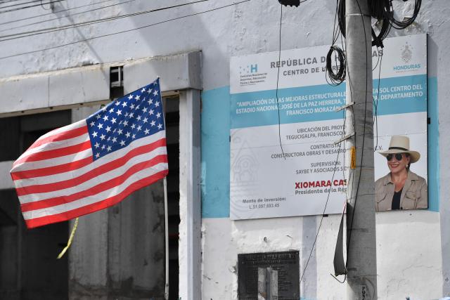 The flags of the United States flutters near a sign depicting Honduras' President Xiomara Castro in Tegucigalpa on December 2, 2025, two days after the national election. Donald Trump accused election officials in Honduras on Monday of "trying to change" their presidential election outcome, as a partial digital tally revealed the two frontrunners are locked in a "technical tie." (Photo by Orlando SIERRA / AFP)