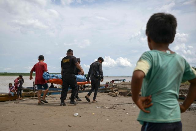Police officers and locals carry the body of one of the victims of a vessel accident at the port of Iparia, in the Ucayali department in Peru's central jungle, on December 2, 2025. At least 12 people, including three children, died when a landslide buried two boats docked at a river port in central Peru, with dozens of others missing, officials said. (Photo by Hugo Alejos / AFP)
