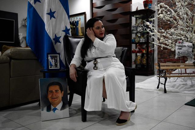 Ana Garcia de Hernandez, wife of former Honduras President Juan Orlando Hernandez, speaks next to a painting of her husband during an interview with AFP in Tegucigalpa on December 2, 2025. Fallen from grace with his former ally, the United States, which sentenced him to 45 years in prison last year, Juan Orlando Hernandez left prison on December 1 amid strong pressure from President Donald Trump over Honduras' presidential elections. (Photo by Orlando SIERRA / AFP)