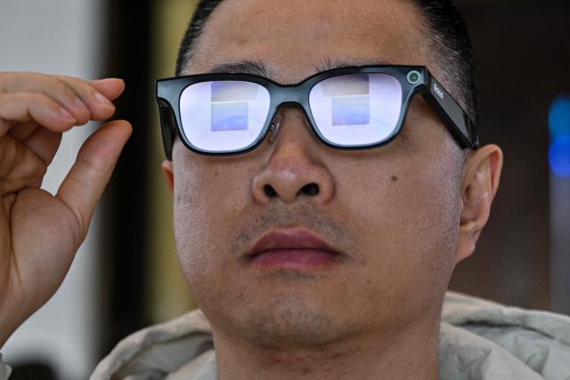 This picture taken on November 13, 2025 shows a man checking a pair of Rokid glasses with display and camera using artificial intelligence (AI) and augmented reality (AR) during a presentation event in Hangzhou, in China's eastern Zhejiang province. In China, AI glasses let the wearer pay in shops with just a glance at a QR code and a voice command, as a growing number of companies look to conquer both growing domestic and overseas markets. Interest in smart eyewear is soaring worldwide after more than a decade of stalled promise, with advances in artificial intelligence sparking renewed interest in the sector. (Photo by Hector RETAMAL / AFP) / To go with 'CHINA-TECHNOLOGY-WEARABLES-AI, FOCUS' by Emily WANG