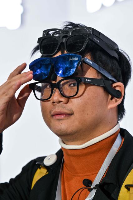 This picture taken on November 13, 2025 shows a man trying on a pair of Rokid glasses with artificial intelligence (AI) during a presentation event in Hangzhou, in China's eastern Zhejiang province. In China, AI glasses let the wearer pay in shops with just a glance at a QR code and a voice command, as a growing number of companies look to conquer both growing domestic and overseas markets. Interest in smart eyewear is soaring worldwide after more than a decade of stalled promise, with advances in artificial intelligence sparking renewed interest in the sector. (Photo by Hector RETAMAL / AFP) / To go with 'CHINA-TECHNOLOGY-WEARABLES-AI, FOCUS' by Emily WANG