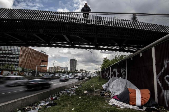 (FILES) A man stands on a pedestrian walkway overlooking migrants's tents lined up the alongside a ring road, underneath a footbridge leading to the Millenaire neighbourhood and the BNP Paribas building at the Porte d'Aubervilliers in Paris on May 10, 2019. In the cold of the early morning, the orange glow of crack pipes under the ring road precedes the arrival of workers from the Millenaire neighbourhood, on the border between north-east Paris and the suburbs. This tense coexistence, against the backdrop of BNP's departure, raises fears of a "ghost neighbourhood". (Photo by Christophe ARCHAMBAULT / AFP)