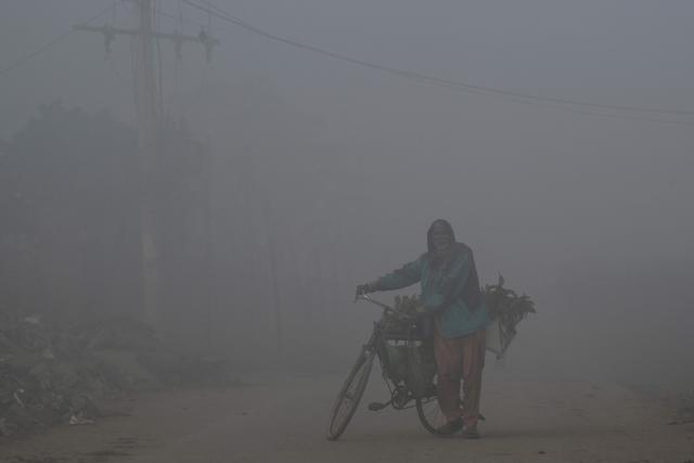 A vendor pushes his bicycle along a street amid dense smog in Lahore on December 3, 2025. (Photo by Arif ALI / AFP)